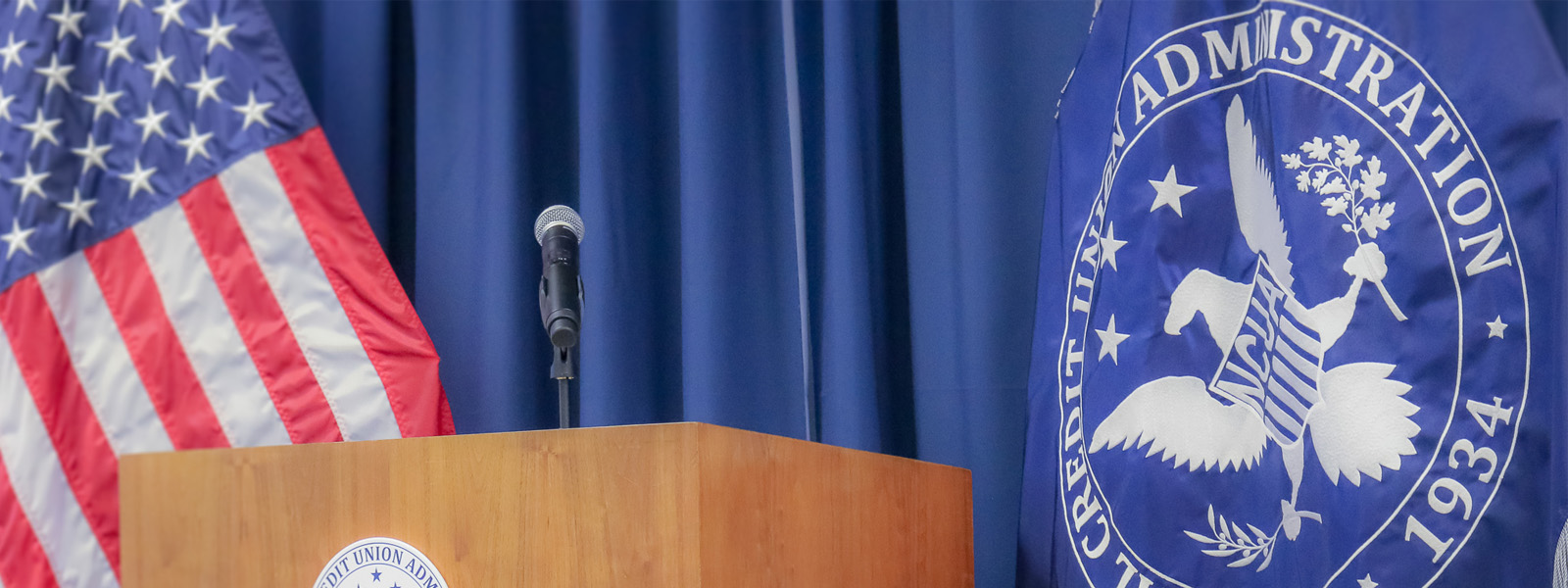 A microphone sits on a podium with the American flag in the background.